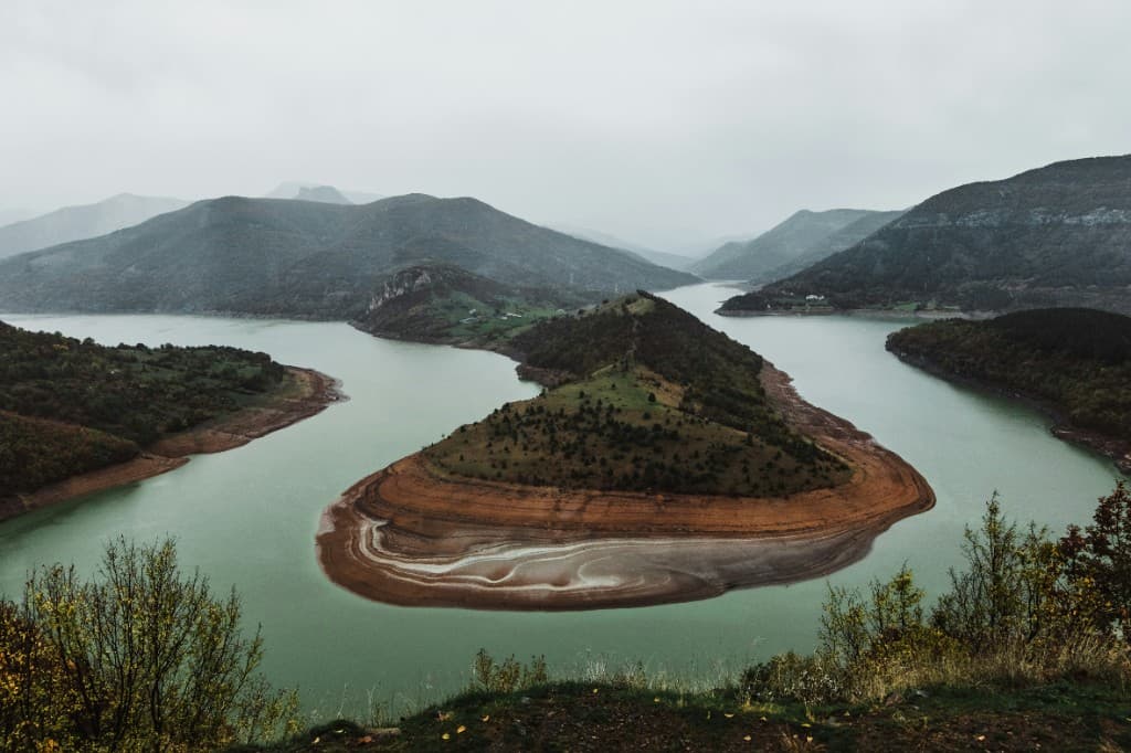 Wide river bend around a forested peninsula under grey sky